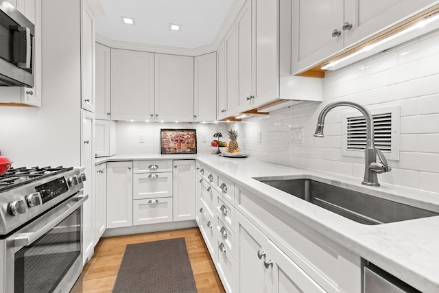 kitchen featuring tasteful backsplash, light hardwood / wood-style floors, white cabinets, and appliances with stainless steel finishes