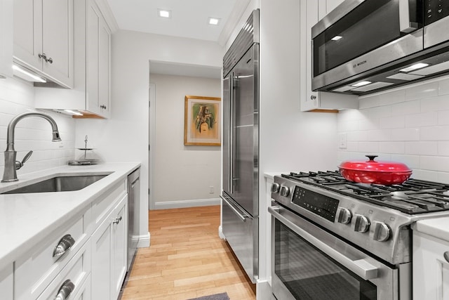 kitchen featuring high quality appliances, tasteful backsplash, light hardwood / wood-style floors, white cabinets, and sink