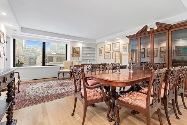 dining area featuring a raised ceiling, built in features, and light hardwood / wood-style floors