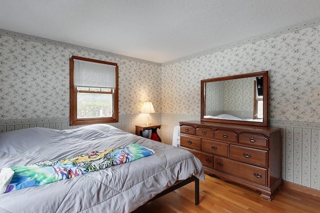 bedroom featuring wallpapered walls, light wood-type flooring, and a textured ceiling