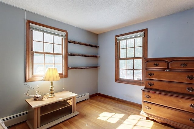 interior space featuring a textured ceiling, a baseboard heating unit, and light wood-style floors