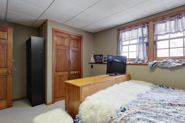 bedroom featuring light colored carpet, baseboards, a closet, and a paneled ceiling