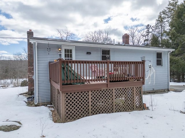 snow covered rear of property with a deck and a chimney