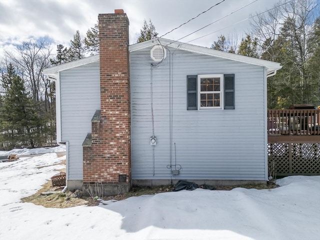 view of snowy exterior with a wooden deck and a chimney