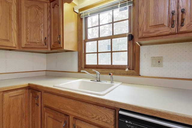 kitchen with a sink, dishwashing machine, brown cabinets, and wallpapered walls