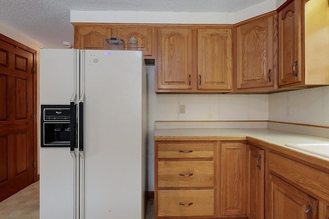 kitchen with light countertops, white refrigerator with ice dispenser, brown cabinets, and a textured ceiling