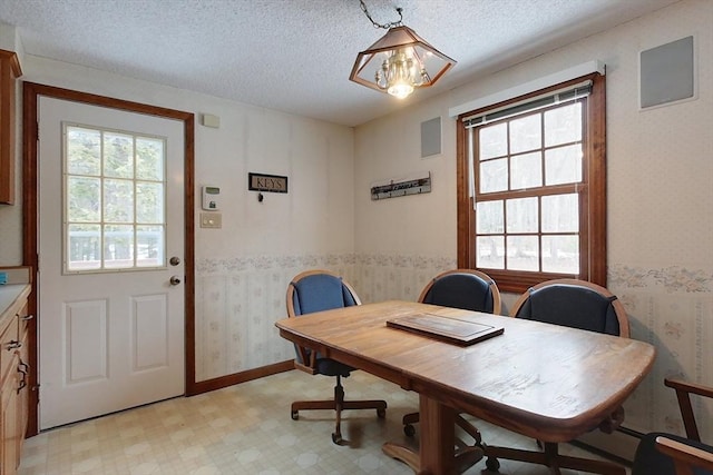 dining space featuring a textured ceiling, light floors, a healthy amount of sunlight, and wallpapered walls