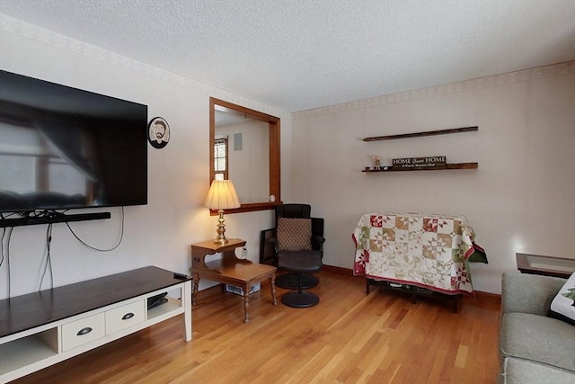 living area with baseboards, a textured ceiling, and wood finished floors