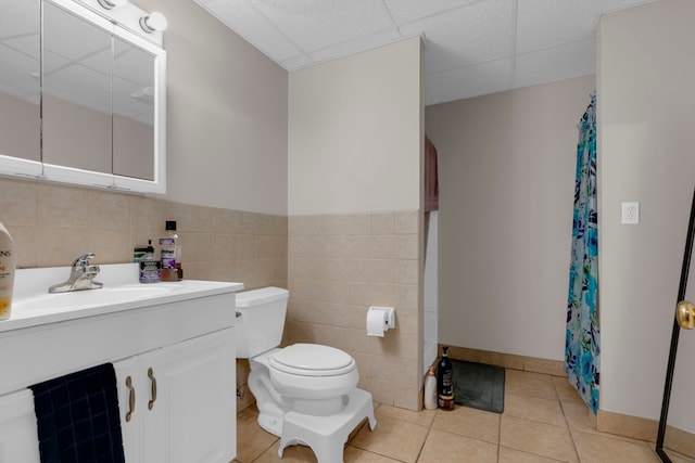 bathroom featuring a paneled ceiling, vanity, tile patterned flooring, toilet, and tile walls