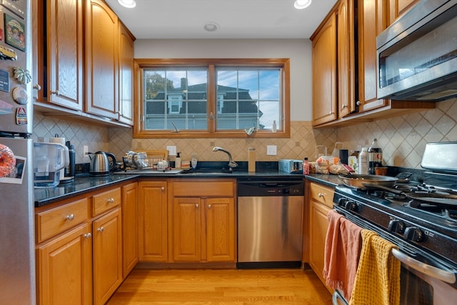 kitchen with sink, stainless steel appliances, backsplash, dark stone counters, and light hardwood / wood-style floors