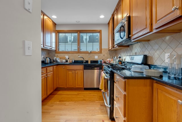 kitchen with light wood-type flooring, tasteful backsplash, stainless steel appliances, sink, and dark stone countertops