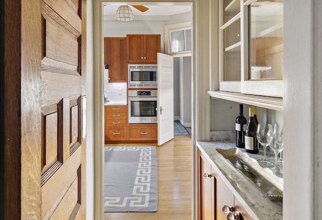 kitchen featuring backsplash, light stone countertops, light hardwood / wood-style flooring, and appliances with stainless steel finishes