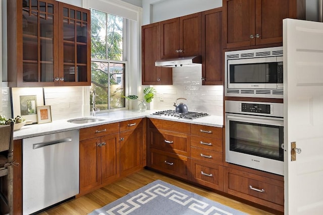 kitchen with light stone countertops, sink, tasteful backsplash, appliances with stainless steel finishes, and light wood-type flooring