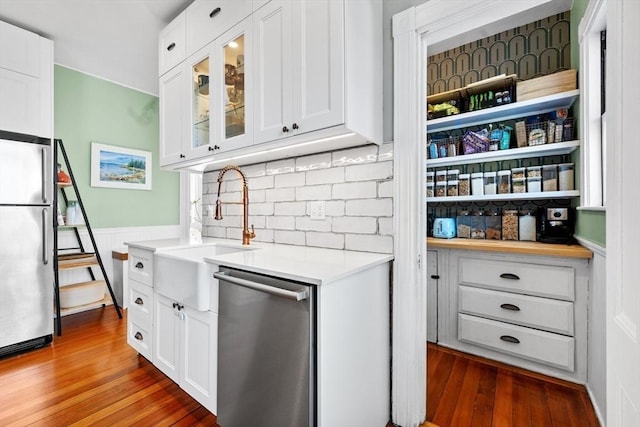 kitchen featuring stainless steel appliances, white cabinets, light countertops, wainscoting, and glass insert cabinets