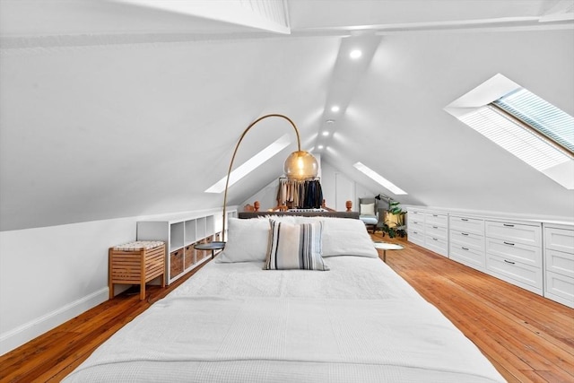 bedroom featuring vaulted ceiling with skylight, baseboards, and wood finished floors