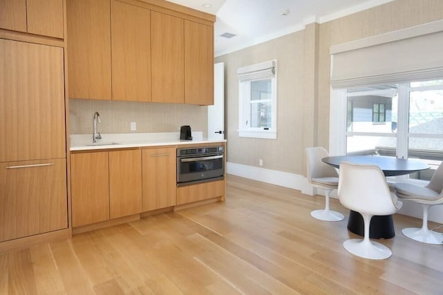 kitchen featuring light wood-type flooring, light brown cabinets, sink, and stainless steel oven