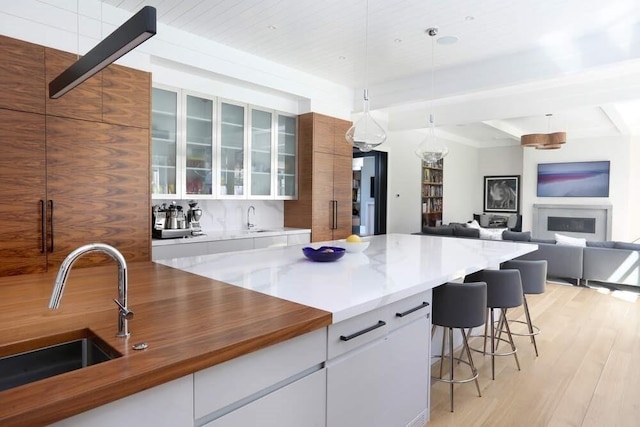 kitchen featuring white cabinets, light wood-type flooring, sink, and hanging light fixtures