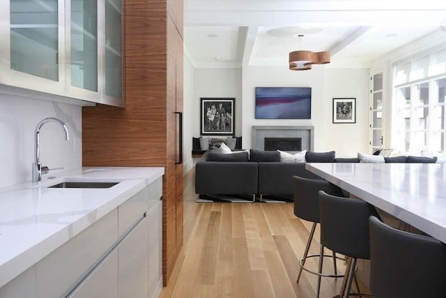 kitchen with light stone countertops, sink, light hardwood / wood-style floors, white cabinetry, and hanging light fixtures