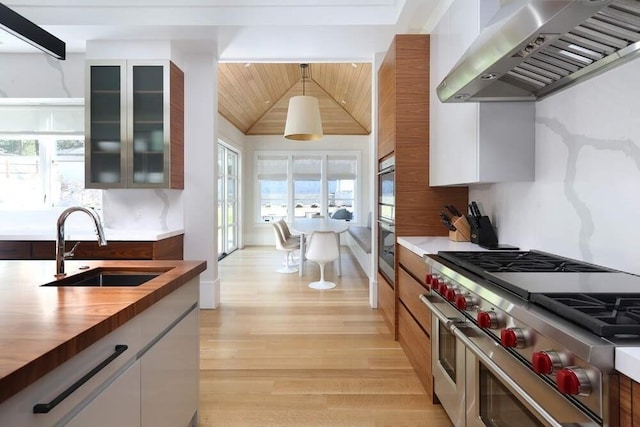 kitchen with sink, range hood, pendant lighting, range with two ovens, and white cabinets