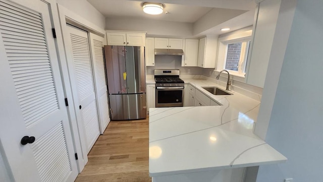 kitchen featuring white cabinets, under cabinet range hood, a sink, light wood-type flooring, and appliances with stainless steel finishes