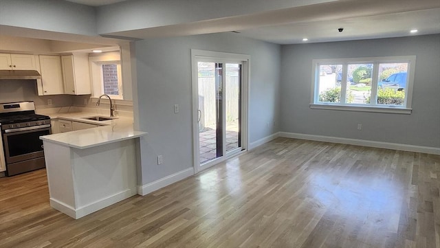kitchen featuring a sink, light wood-style floors, gas range, light countertops, and under cabinet range hood
