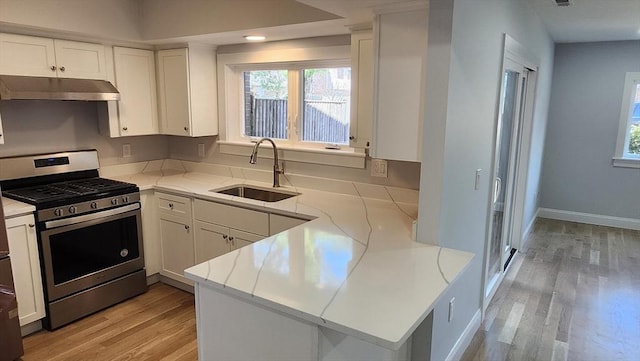 kitchen featuring white cabinets, under cabinet range hood, a sink, gas range, and light wood-style flooring