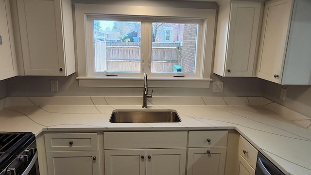 kitchen featuring gas range oven, white cabinetry, a sink, and light countertops