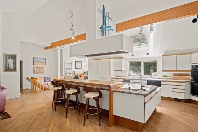 kitchen featuring track lighting, high vaulted ceiling, light hardwood / wood-style floors, and white cabinets