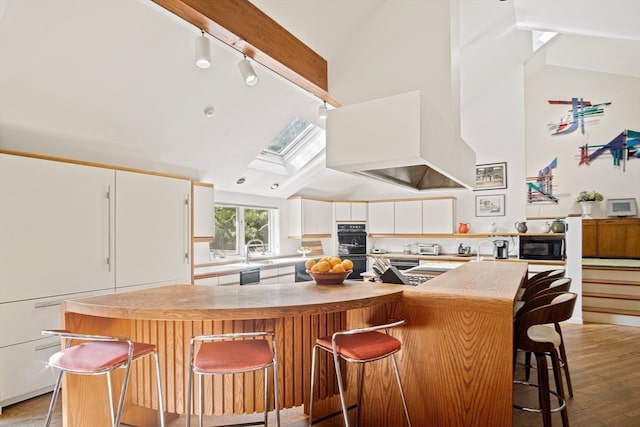 kitchen with white cabinets, a skylight, high vaulted ceiling, a breakfast bar, and light hardwood / wood-style floors