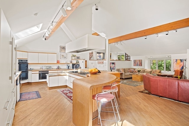 kitchen featuring light wood-type flooring, white cabinetry, a kitchen breakfast bar, high vaulted ceiling, and track lighting