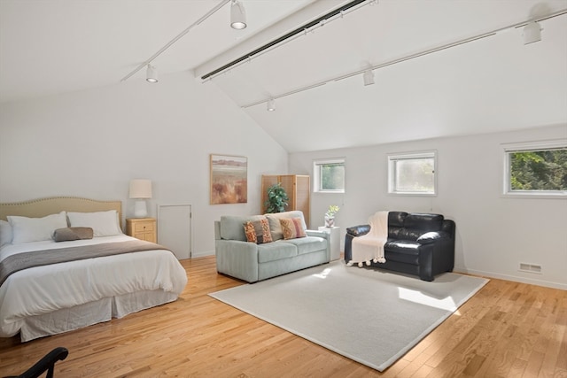 bedroom featuring light hardwood / wood-style floors, beam ceiling, track lighting, and high vaulted ceiling