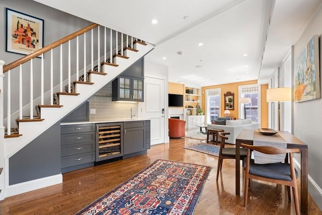 indoor wet bar with wine cooler, wood finished floors, stairs, baseboards, and recessed lighting