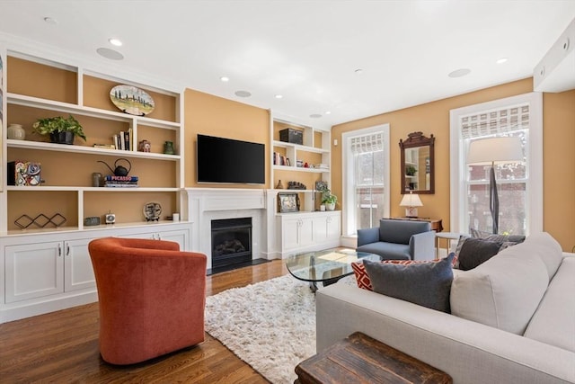 living area featuring dark wood-style flooring, a fireplace with flush hearth, built in shelves, and recessed lighting