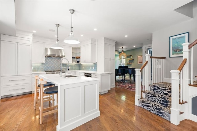 kitchen featuring range hood, light countertops, decorative backsplash, light wood-type flooring, and recessed lighting