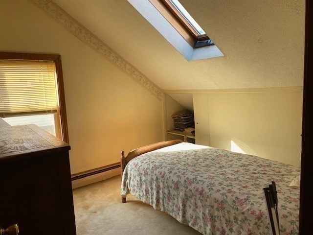 bedroom featuring light carpet, a baseboard heating unit, a textured ceiling, and vaulted ceiling