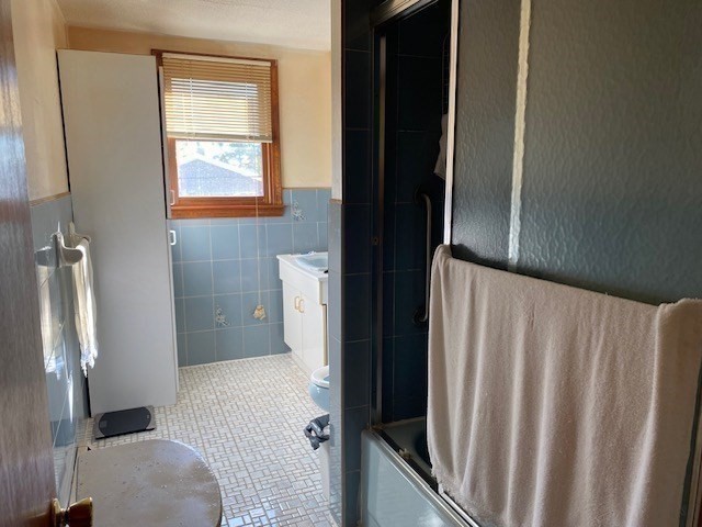 full bathroom featuring combined bath / shower with glass door, toilet, tile walls, vanity, and tile patterned flooring