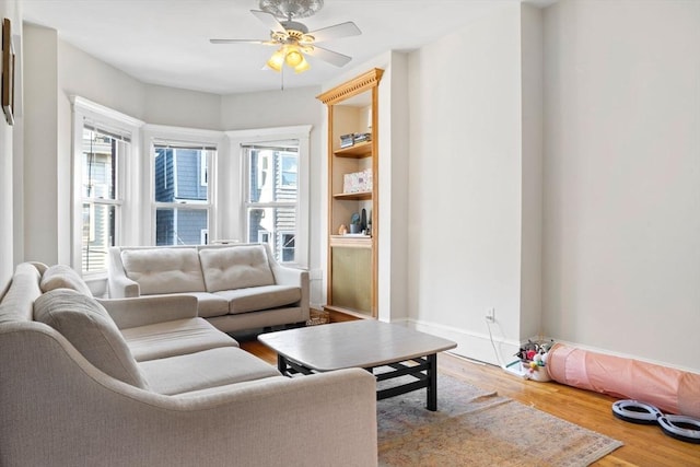 living room featuring built in shelves, wood-type flooring, and ceiling fan