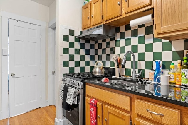 kitchen featuring sink, light hardwood / wood-style flooring, stainless steel range with gas cooktop, dark stone counters, and decorative backsplash