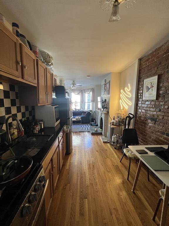 kitchen with sink, ceiling fan, stainless steel appliances, light hardwood / wood-style floors, and brick wall