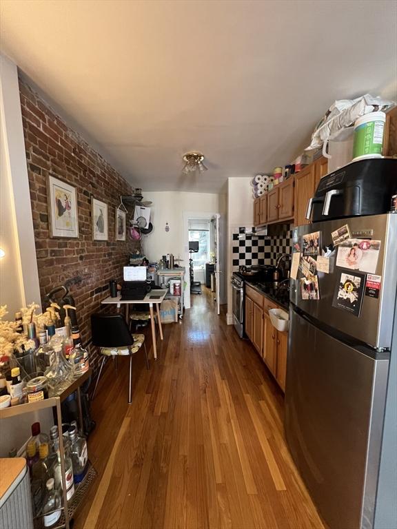 kitchen with decorative backsplash, brick wall, appliances with stainless steel finishes, and light hardwood / wood-style flooring