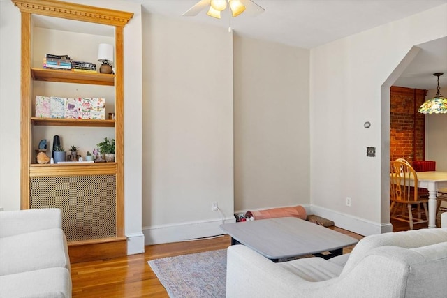 living room with built in shelves, ceiling fan, and light hardwood / wood-style flooring