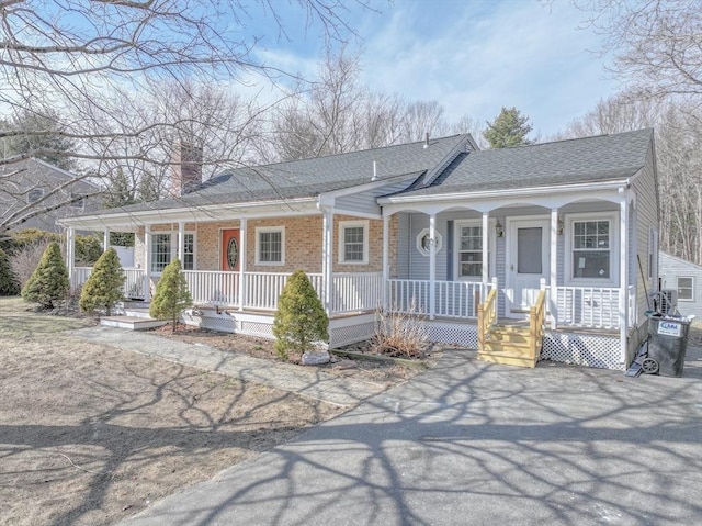 view of front of property featuring covered porch, a shingled roof, a chimney, and brick siding