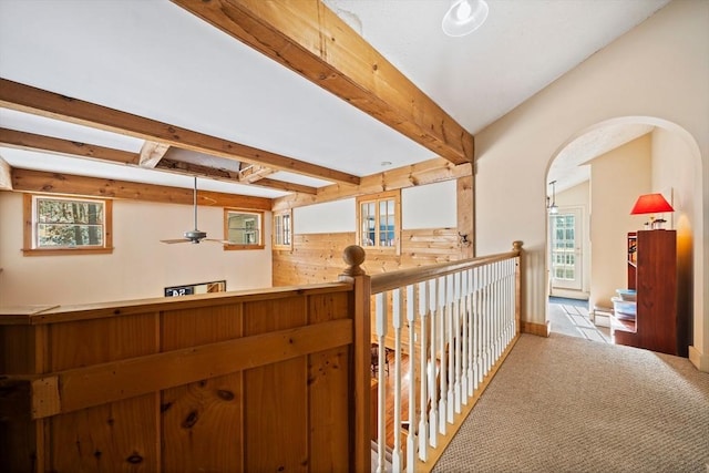 corridor featuring light carpet, wood walls, plenty of natural light, and beamed ceiling