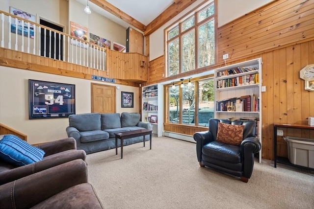 living room featuring a baseboard radiator, a high ceiling, a healthy amount of sunlight, carpet floors, and wooden walls