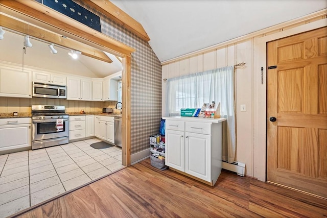 kitchen with white cabinets, a baseboard radiator, appliances with stainless steel finishes, and lofted ceiling