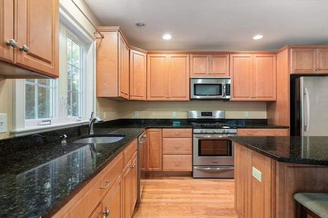 kitchen featuring appliances with stainless steel finishes, light hardwood / wood-style floors, sink, and dark stone counters