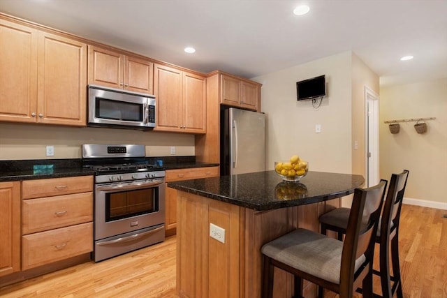 kitchen with a breakfast bar, stainless steel appliances, a kitchen island, dark stone counters, and light wood-type flooring