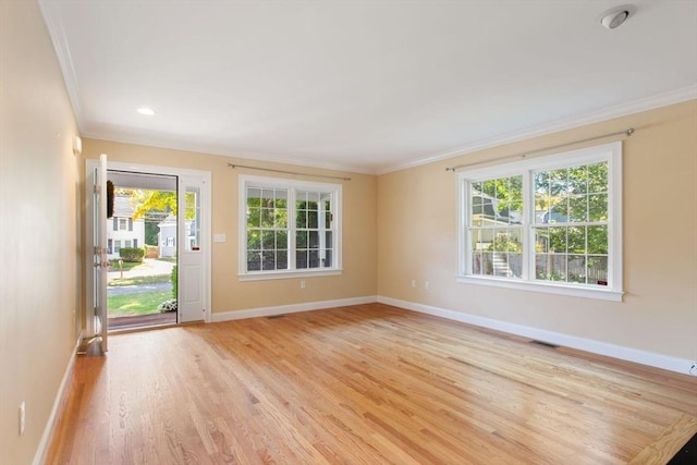 empty room featuring a healthy amount of sunlight, ornamental molding, and light hardwood / wood-style flooring