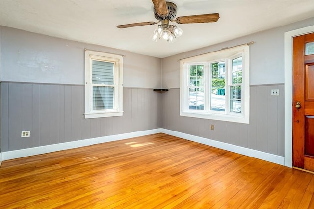 empty room featuring light wood finished floors, ceiling fan, wainscoting, wood walls, and baseboards