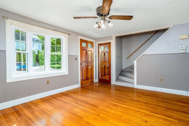 foyer with light wood finished floors, baseboards, stairs, a wainscoted wall, and ceiling fan